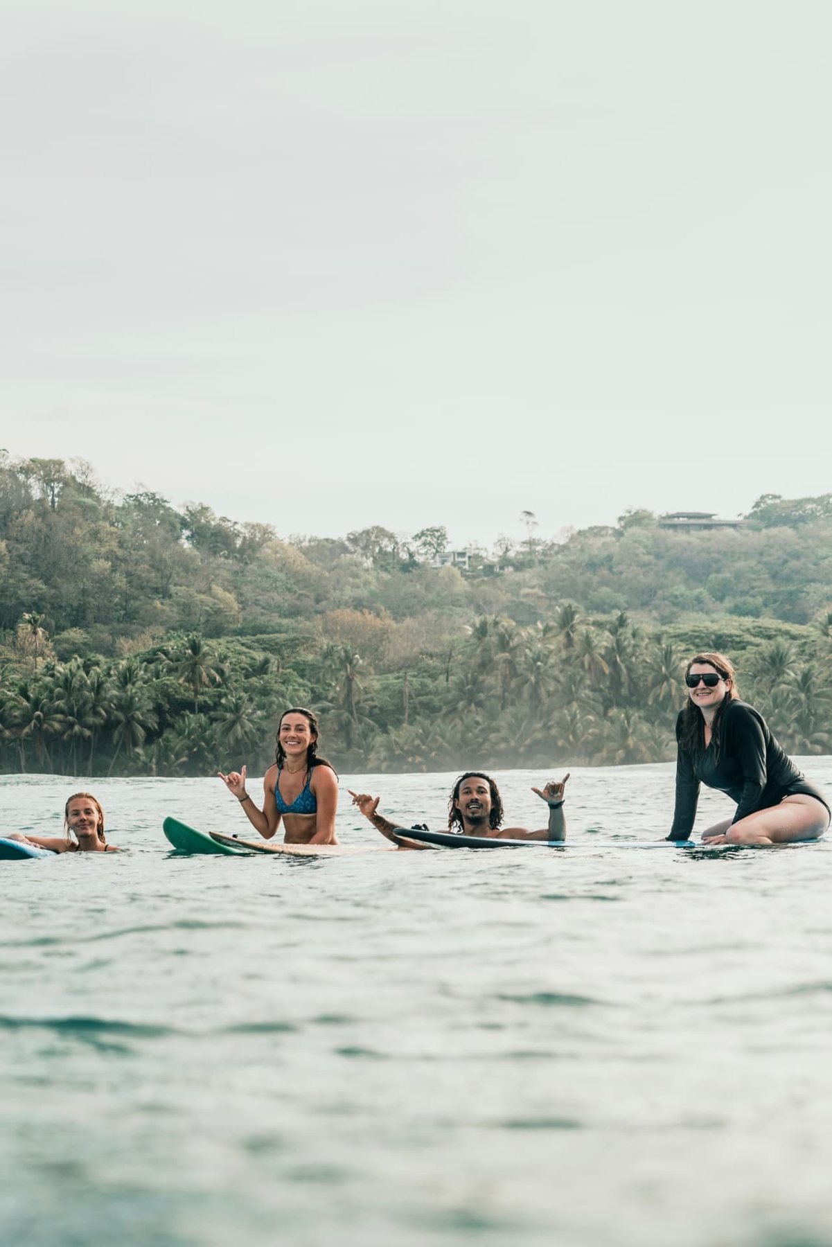Four surfers throwing shakas in the lineup with the jungle behind them in Santa Teresa
