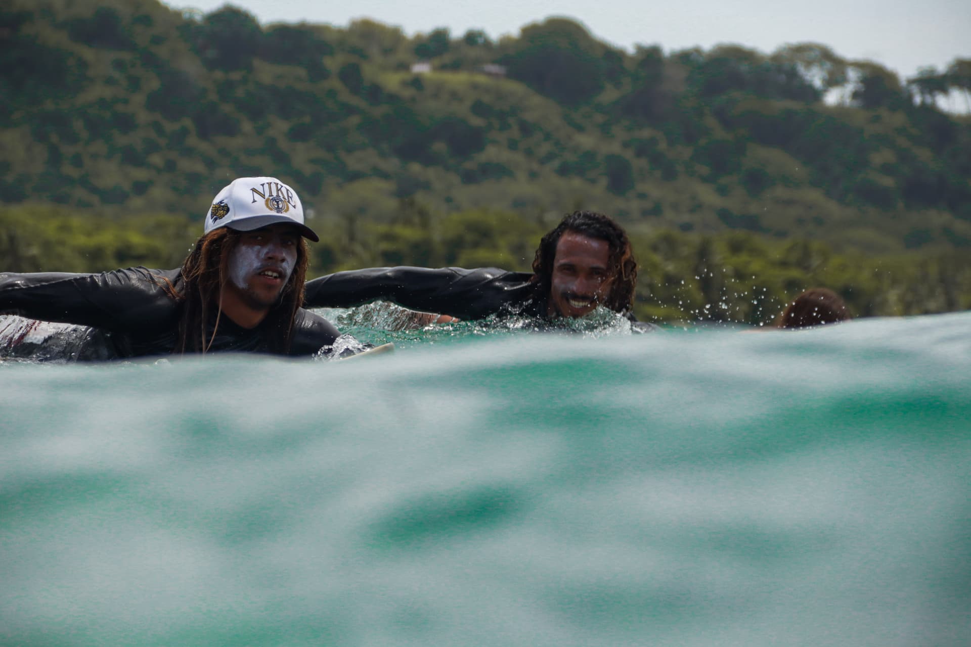 Two Beach Boys surf coaches paddling out through green water in Santa Teresa, Costa Rica
