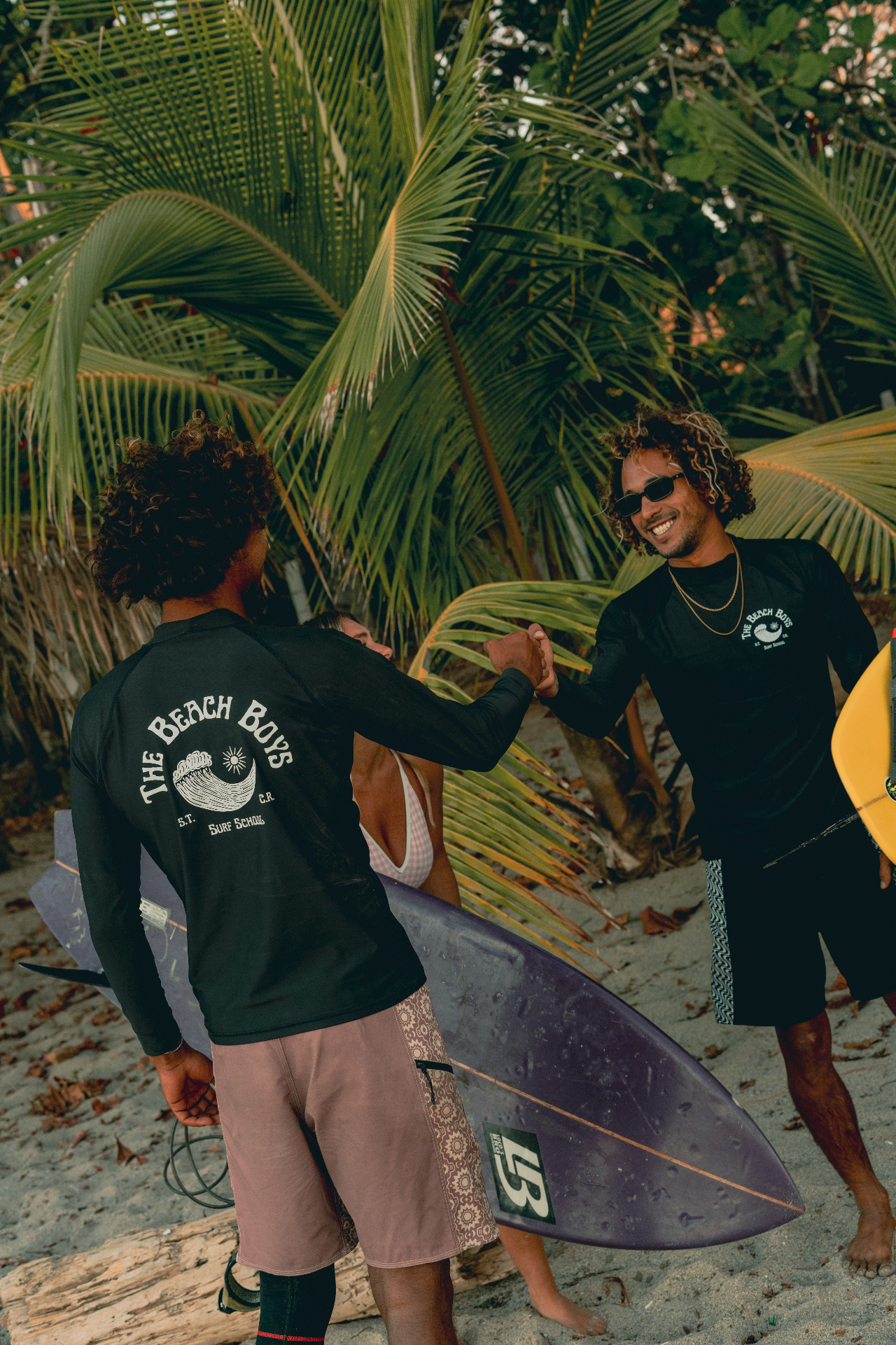 Isaac, founder and head coach at The Beach Boys, sharing a fist bump with a local surfer under the palms in Santa Teresa