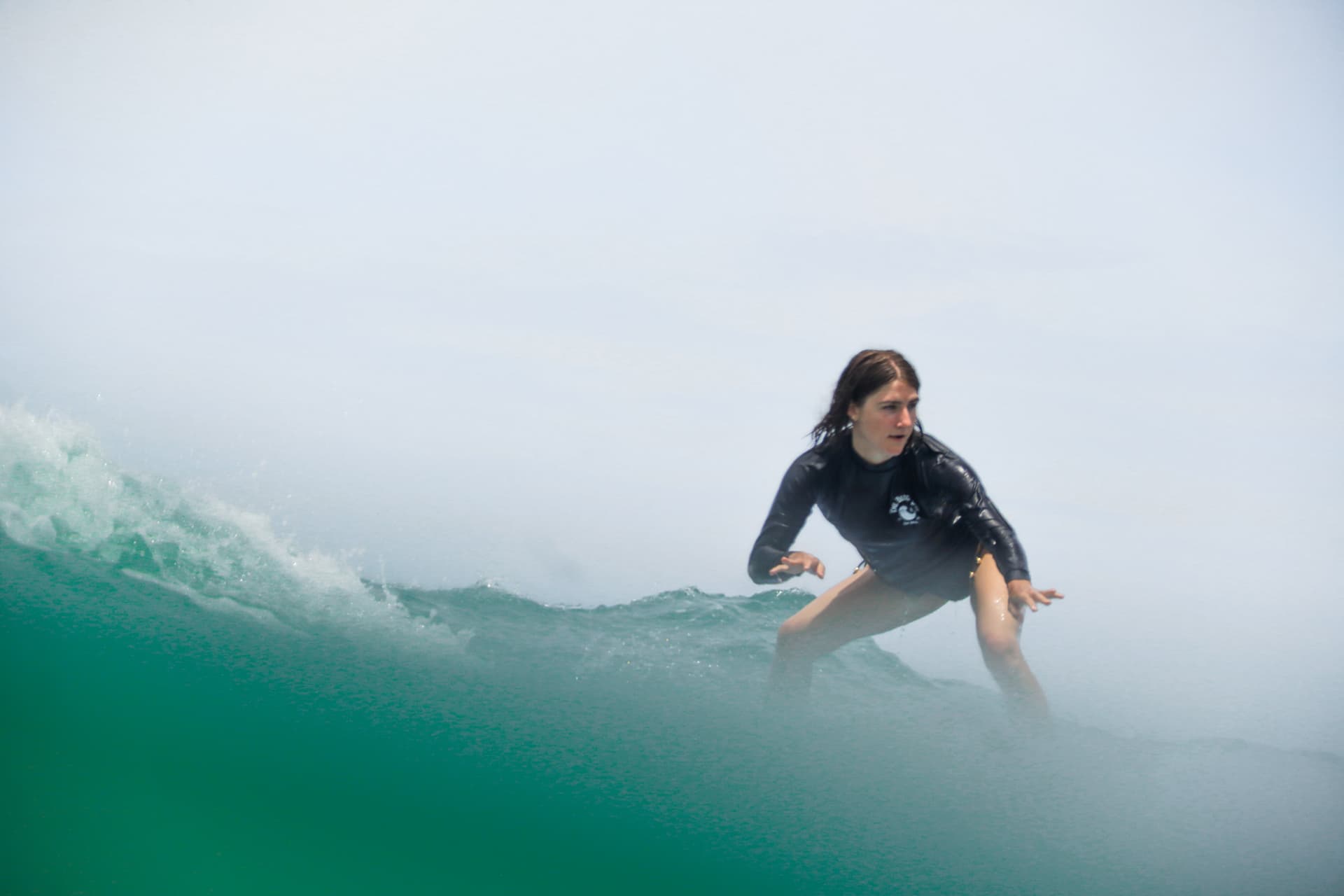A surfer in a Beach Boys rash guard riding across a clean green wave in Santa Teresa