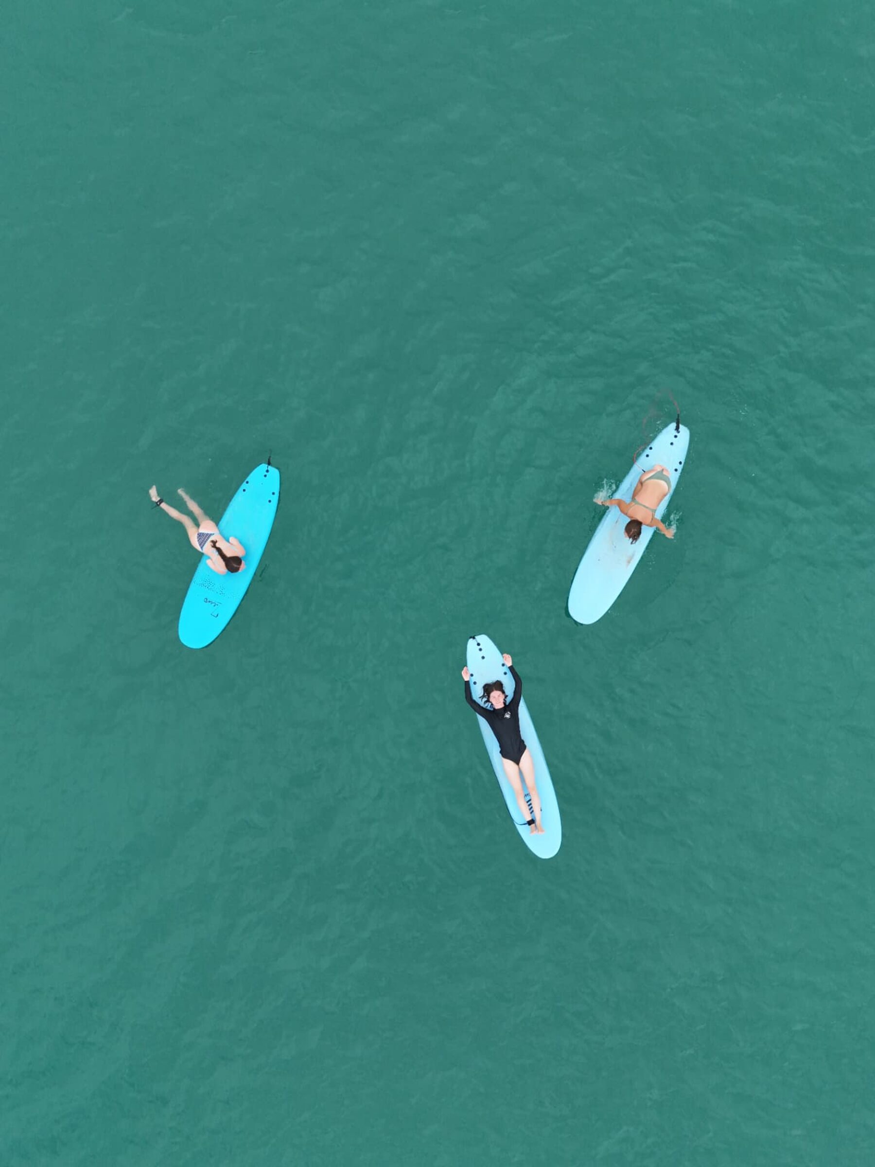 Aerial view of three surfers resting on longboards in turquoise water in Santa Teresa