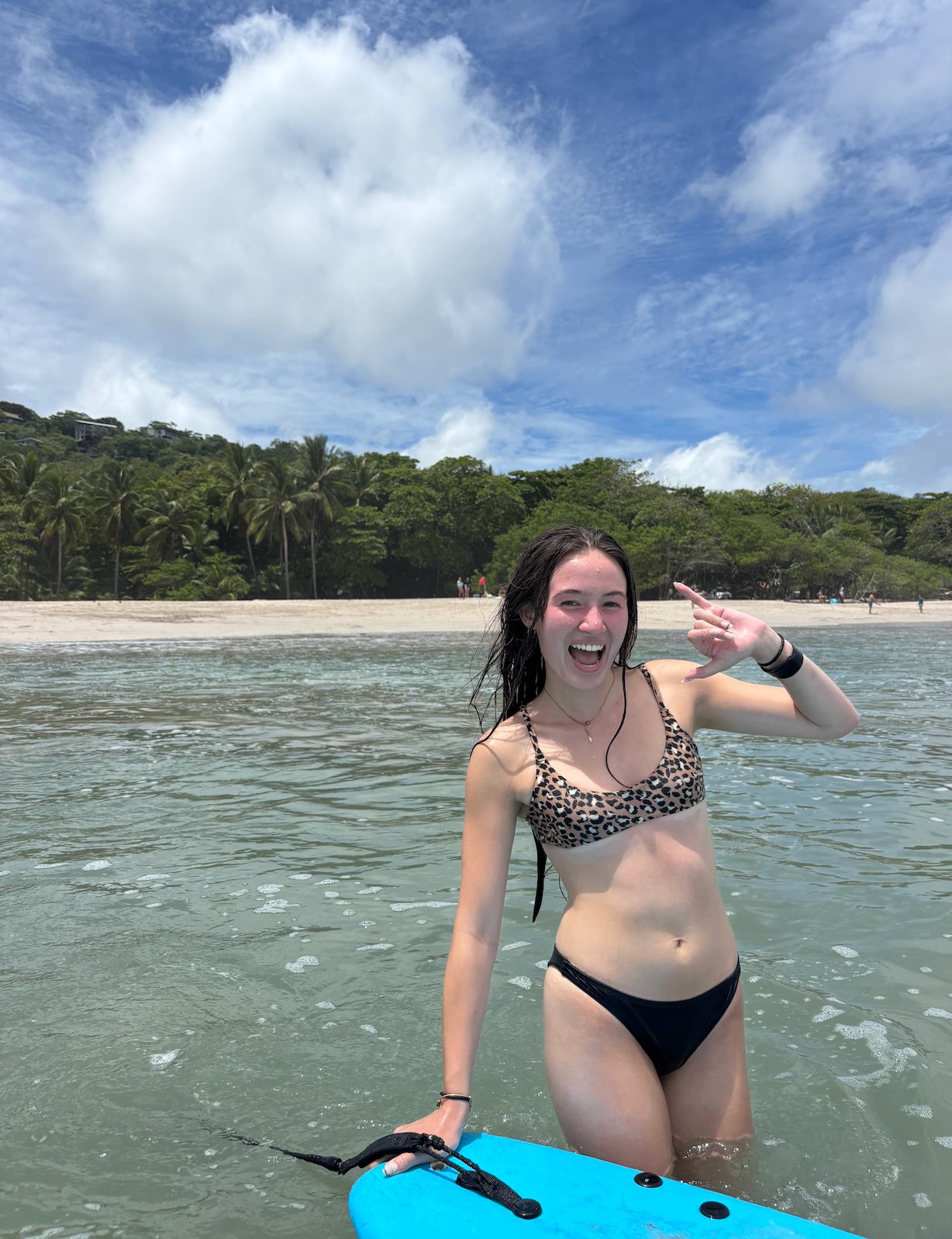 A grinning beginner walking her board back out after catching a wave in Santa Teresa
